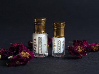 Concentrated perfume in a mini bottle with floral petals on the black table - obrazy, fototapety, plakaty