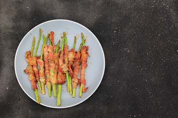 Grilled bacon wrapped green asparagus on dark background