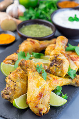 Indian chicken tandoori, marinated in greek yogurt  and spices, served with lime wedges and cilantro on slate plate, vertical