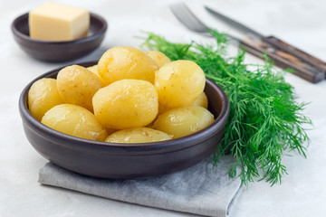 New young boiled potato topped with melted butter in ceramic bowl and dill on background, horizontal