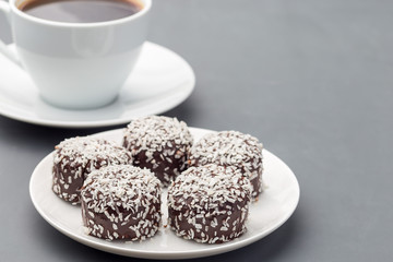 Swedish sweets chocolate balls or chokladbollar, made from oats, cocoa, butter and coconut, on white plate, served with coffee,  horizontal, copy space