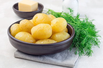 New young boiled potato topped with melted butter in ceramic bowl,   dill on a background, horizontal