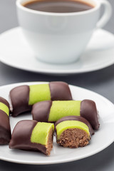 Swedish sweets punsch rolls or punschrullar, covered with green marzipan, on a white plate, served with coffee,  vertical