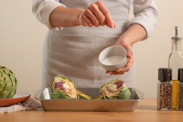 Chef salt and prepare to bake the artichoke on a light background, the concept of cooking tasty and healthy food, menus, recipe book, detox, Organic produce or local market concept