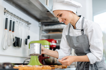 Patissier putting cocoa powder on little cakes