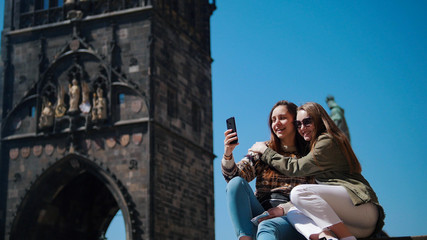 Fototapeta na wymiar Two young women huging and take a selfie on the background of the historic tower