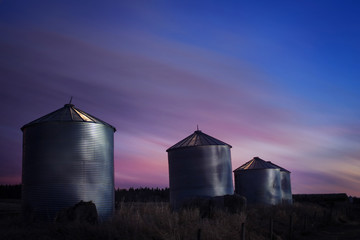 Grain silos on farmland silhouetted by a sunset. Alberta