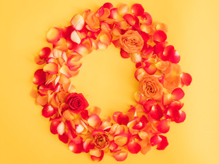 Floral wreath. Red rose buds and petals arranged in round frame over orange background. Copy space.