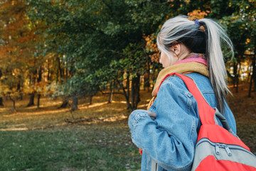 Fototapeta na wymiar Country tourism. Lady hiking with backpack in autumn nature park. Blur trees and foliage background.