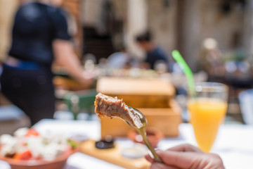 Sliced grilled lamb chops on a fork. Woman have a dinner in a greek tavern