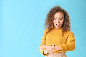 Beautiful African-American woman looking at watch against color background