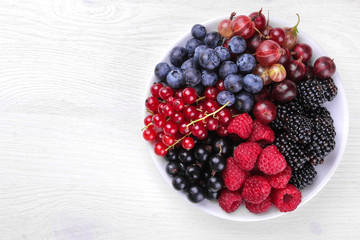Delicious berries in a bowl, currants, blackberries, blueberries, raspberries on a white wooden table. top view
