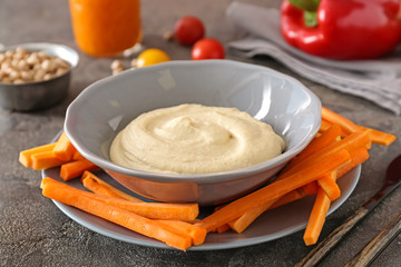 Bowl of tasty sauce and fresh carrot on grey table