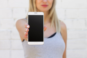 The girl is holding a mobile phone with a blank black screen on an outstretched arm close up. Mockup smartphone for the presentation of the design
