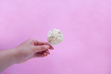 female hand holding a measuring spoon of whey protein powder with plastic spoon on pink background