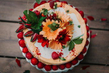Rustic naked cake with strawberries, white cream and flower decoration on a wooden table