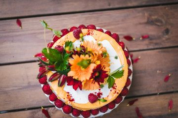 Rustic naked cake with strawberries, white cream and flower decoration on a wooden table