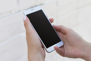 Female hand holding smartphone on white brick wall background, mockup with copy space. Phone with a blank screen for design