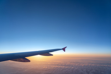 Fototapeta premium Up in the air, view of aircraft wing silhouette with dark blue sky horizon and cloud background in sunset time, viewed from airplane window