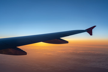 Naklejka na ściany i meble Up in the air, view of aircraft wing silhouette with dark blue sky horizon and cloud background in sunset time, viewed from airplane window