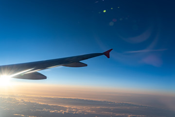 Fototapeta premium Up in the air, view of aircraft wing silhouette in dark blue sky horizon and cloud background in sunset time. viewed from airplane window, with a reflection camera lens