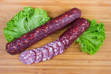 Partly sliced dry-cured sausages with lettuce on cutting board