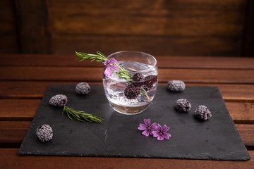 gin and tonic with blackberries, a sprig of rosemary and a flower of ornament