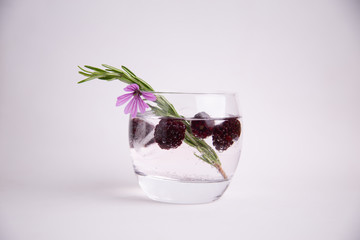 gin and tonic with blackberries, a sprig of rosemary and a flower of ornament