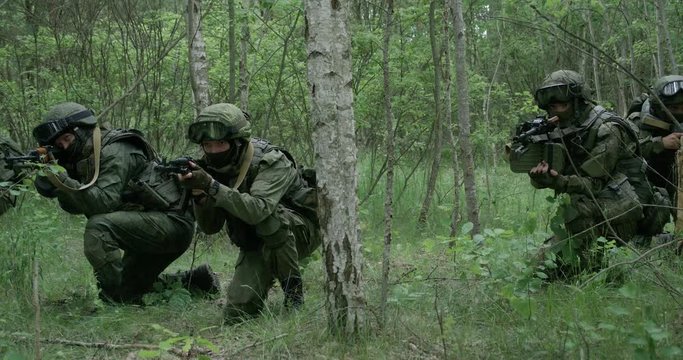 Soldiers in camouflage with assault rifle walking through the forest, military action in the woods, 4k slow motion.