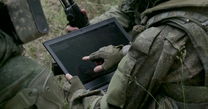 Soldiers in camouflage in ambush, military engineer uses a laptop navigation system, military action in the steppe area.