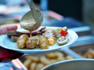 Celebration event with catering table and a woman's hand with plate. person in line with their food during a banquet. meat beef vegetables and grilled potatoes. Food Buffet Catering Eating Concept