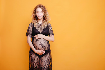pregnant young beautiful fashion blonde model woman in studio in black underwear on yellow orange background copy space