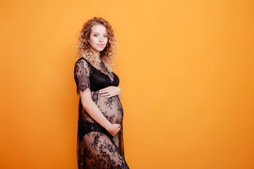 Fototapeta premium pregnant young beautiful fashion blonde model woman in studio in black underwear on yellow orange background copy space