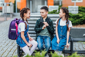 Obraz premium Pupils of primary school. Girls and boy with backpacks near building outdoors. Beginning of lessons. First day of fall.
