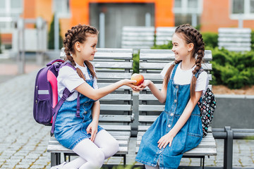 Photo of  beautiful two  small daughter giving red apple, study time see you soon.