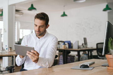 Young businessman sitting at his desk using a digital tablet