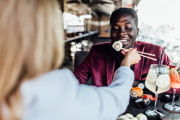 Photo of the back, blonde woman feeding her boy sushi rolls in summer terrace.