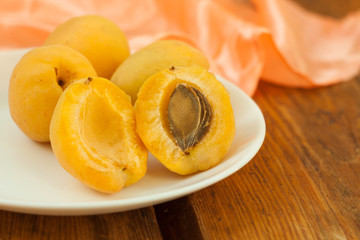 Ripe fresh apricot fruits halvs on a white plate on the wooden background. Copy space, delisious healthy food.