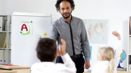 Tilt up shot of little schoolboy sitting at his desk and raising hand to answer question of male Arab primary school teacher teaching alphabet in class - Powered by Adobe
