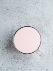 Obraz na płótnie Canvas Trendy drink: pink latte. Beetroot or raspberry cappuccino or latte in glass cup on gray cement background. Copy space for text. Vertical. Top view or flat lay.