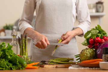The chef cleans and cuts asparagus, with vegetables on a light background. The concept is loss of healthy and healthy food, detox, vegan food. Slow food, comfort food, clean food