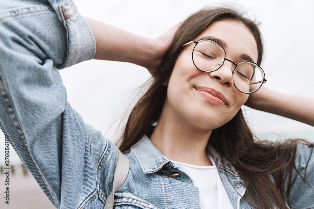 Wall mural Happy young pretty woman student wearing eyeglasses walking outdoors resting.