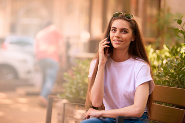 Beautiful young woman relaxing on the bench and making a call