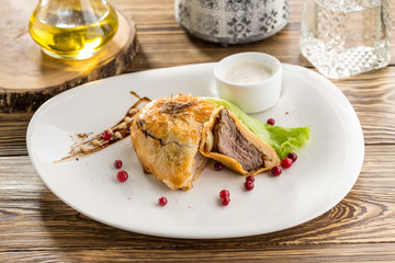 Beef wellington with cranberry and white sauce on wooden table