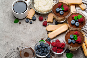 Frame made of Classic tiramisu dessert with blueberries and raspberries in a glass and savoiardi cookies on concrete background