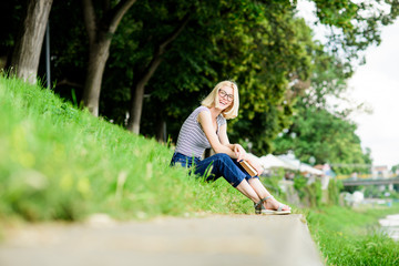 Naklejka na ściany i meble Woman dreaming about vacation. Literature for summer vacation. Girl relaxing at riverside after working day. Rest relax and hobby. Summer vacation. Girl sit on green grass near river and read book