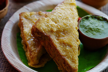 Sandwich Bread Pakora / pakoda (triangle shape) served with tomato ketchup, chutney, green chilli and onion slices, Popular indian tea-time snack