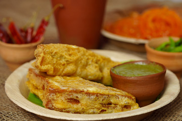 Sandwich Bread Pakora / pakoda (triangle shape) served with tomato ketchup, chutney, green chilli and onion slices, Popular indian tea-time snack