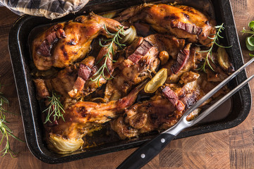 Portioned baked rabbit in a pan with onion rosemary and sauce