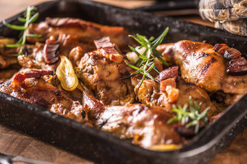 Portioned baked rabbit in a pan with onion rosemary and sauce